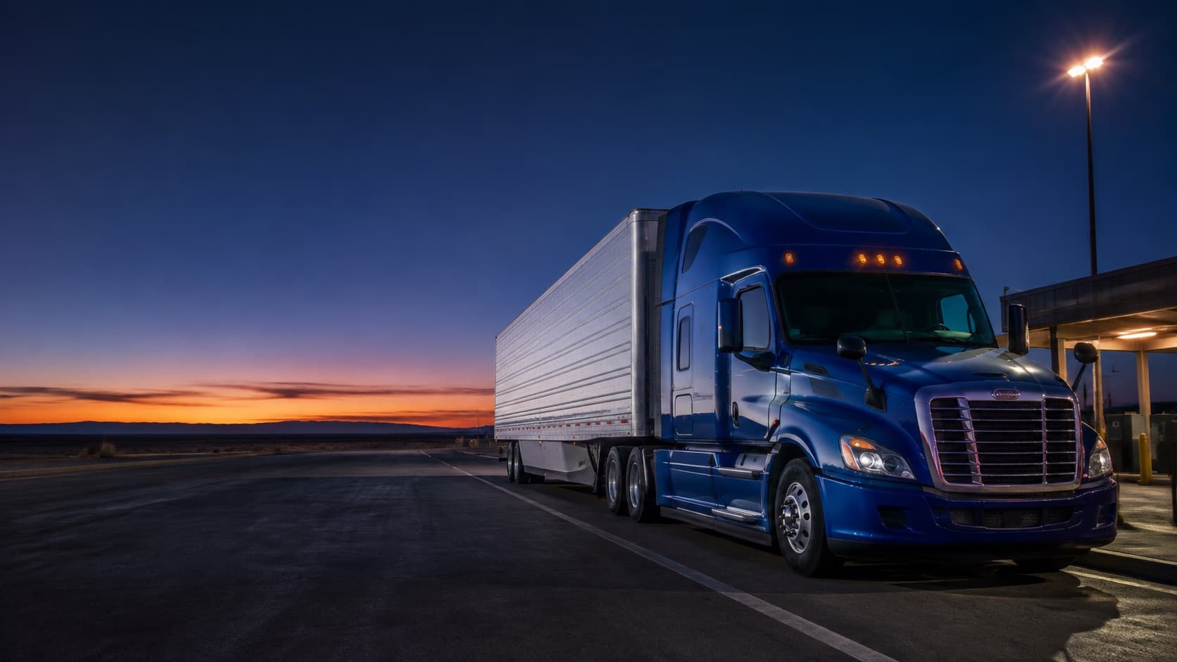 Blue semi truck and trailer parked before sunrise